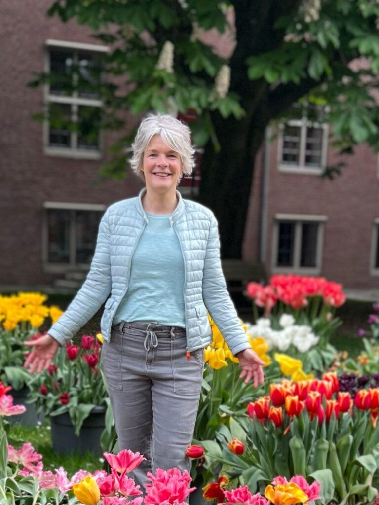 Biografisch coach Jeanine Streng van coachingpraktijk Tot hier en verder, poserend tussen de tulpen.