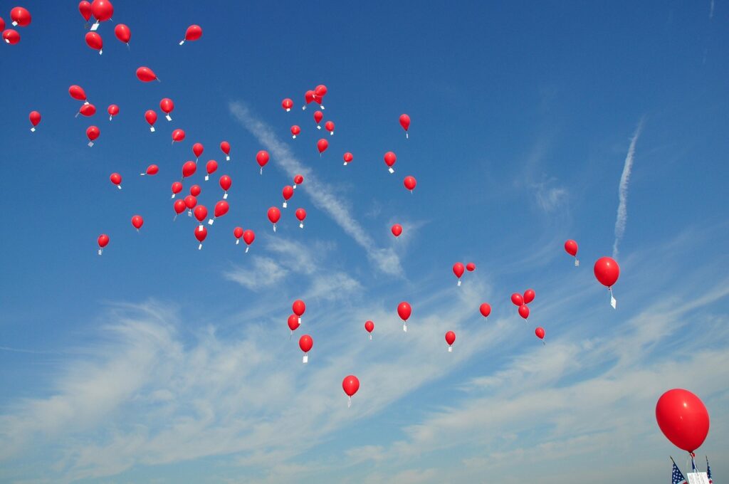 Rode ballonnen in de lucht met een kaartje eraan als symbool voor loslaten en outplacement