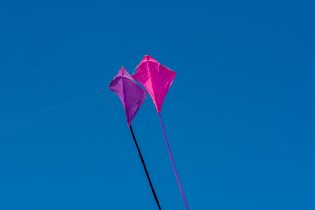 Bright pink and purple kites flying high in a clear blue sky, symbolizing freedom and joy.